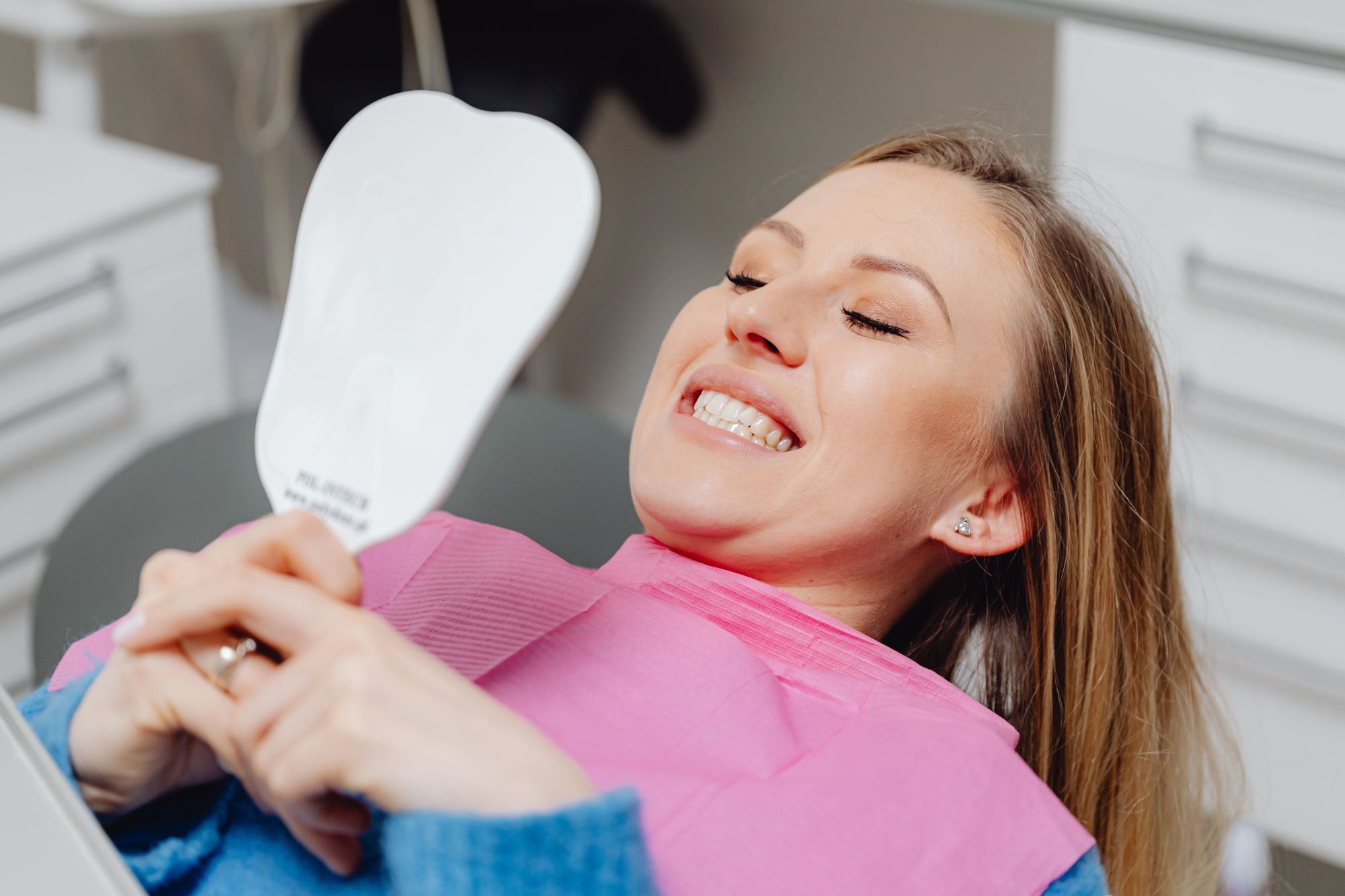 Smiling dental patient looking in a mirror after discussing cosmetic smile options